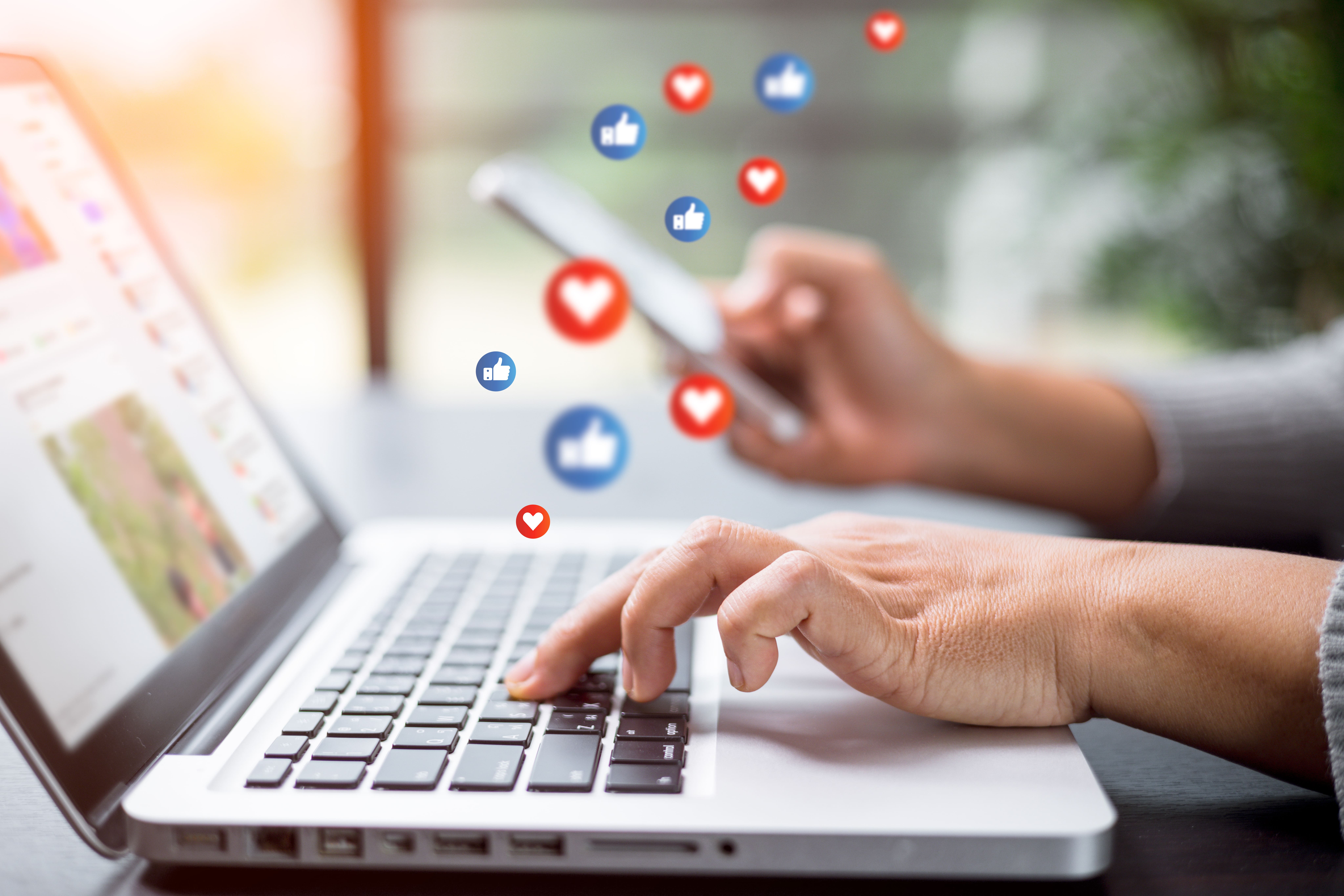 Person using a laptop and smartphone with floating social media like and heart icons, representing social media engagement for retailers.