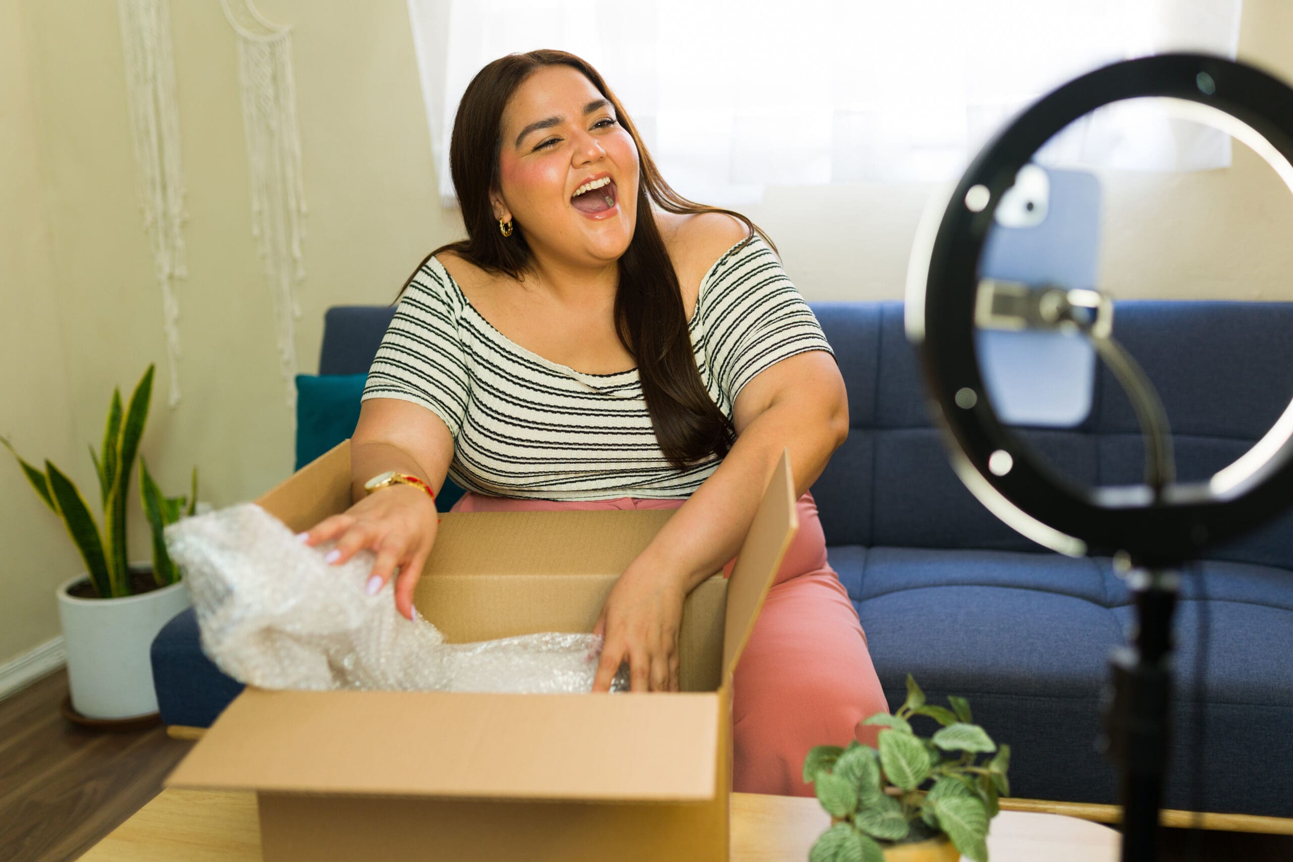 The Death of Hashtag Marketing (And What Actually Works Now) Smiling woman recording an unboxing video at home with a smartphone and ring light, highlighting video marketing and authentic user-generated content, not hashtag marketing.