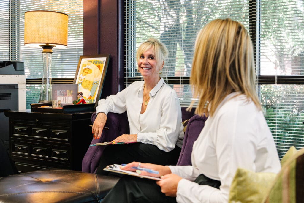 We Discover What's Next in AI Marketing Tools Two women in a modern, professional office having a marketing strategy meeting at Creative Marketing Arts, with vibrant decor and natural light.