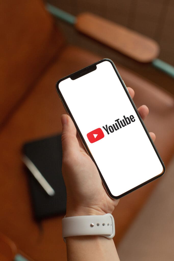 We Discover What's Next in YouTube Algorithm & Video Marketing Person holding a smartphone with YouTube logo on the screen, representing YouTube video marketing strategy in 2025.