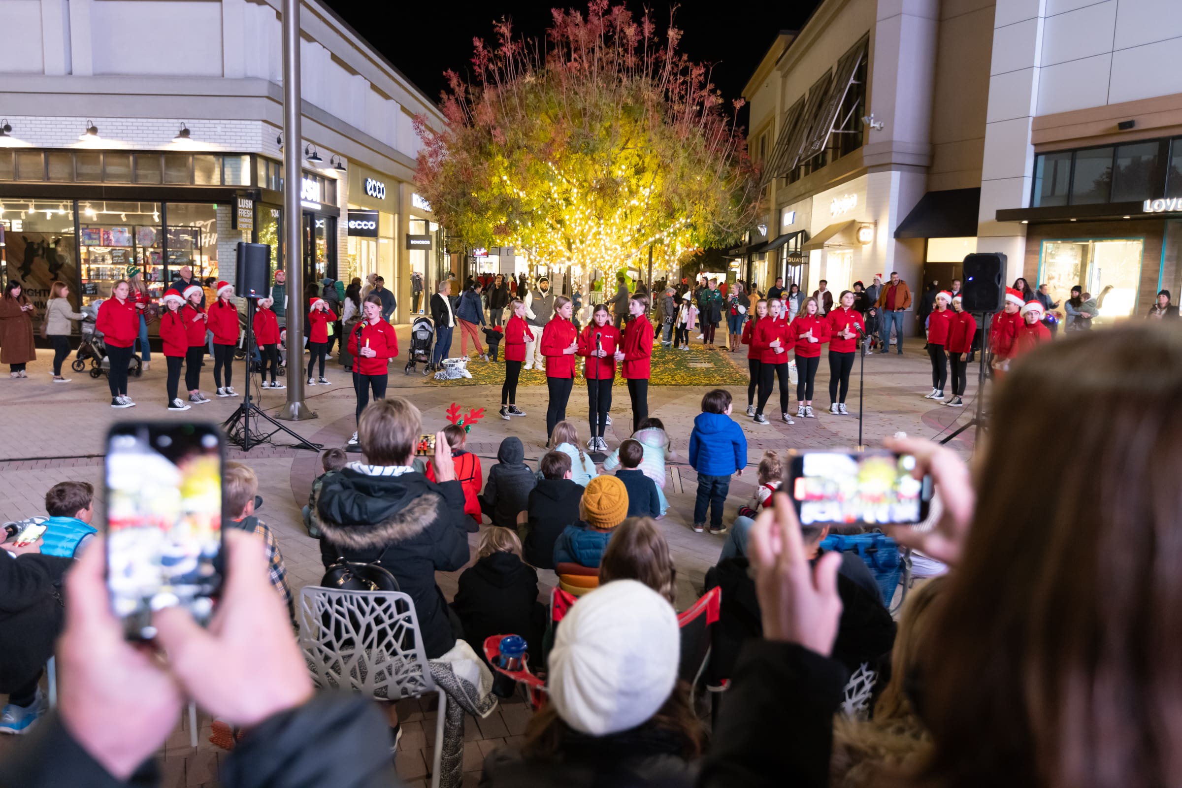 Holiday experiential retail event with community gathered around a decorated tree.