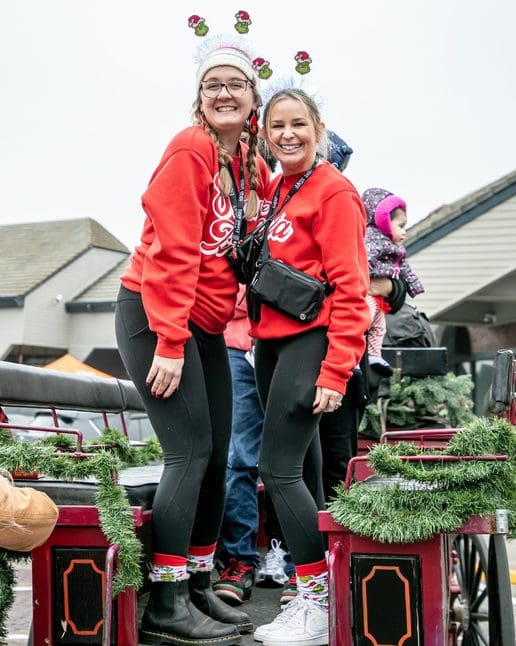 Two women smiling during a season of celebration while participating in a holiday parade at Loehmann’s Plaza