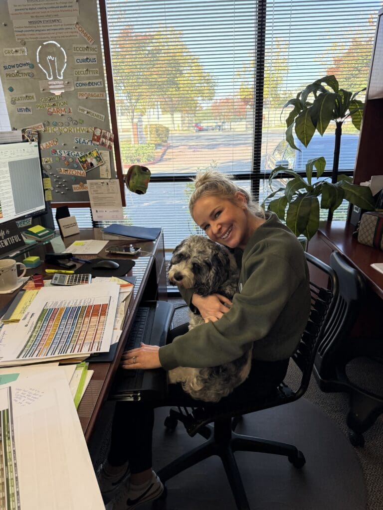 Kids and Dogs in Social Media Marketing Are the Secret Sauce for High Engagement Woman working at her desk while holding a small dog, an example of authentic office moments that enhance engagement in kids and dogs in social media marketing.