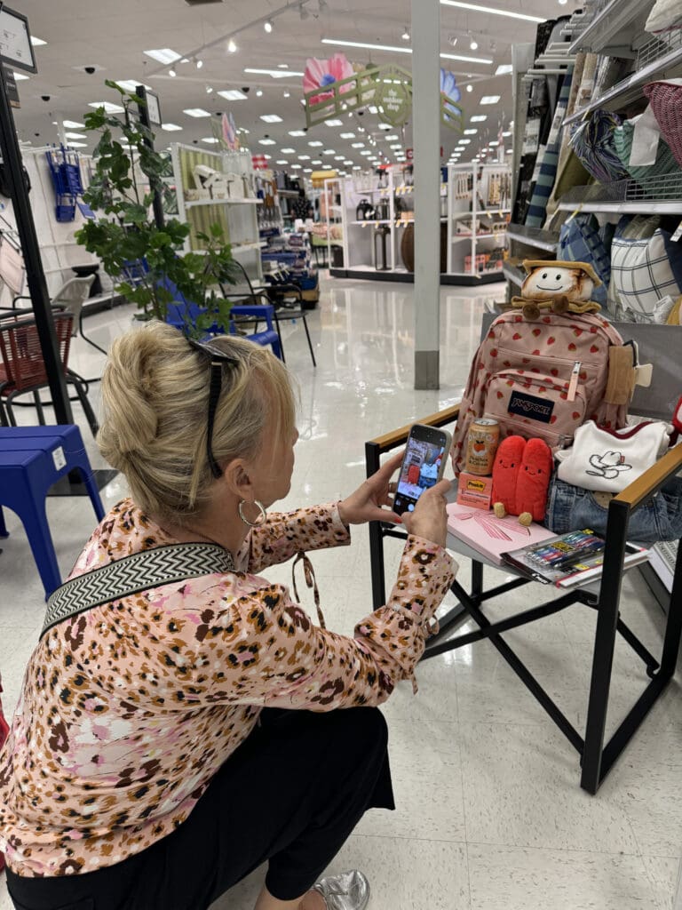 Authentic Social Media Marketing Blonde woman photographing some back to school items including pens, a notebook, a backpack, post-its, and clothes.