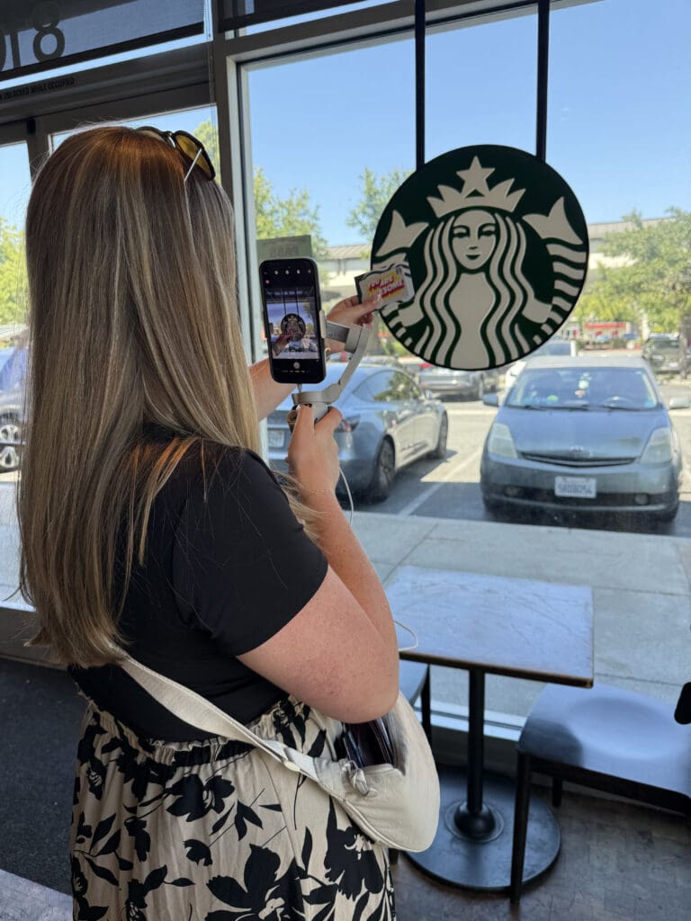Authentic Social Media Marketing Blonde woman holding phone taking picture of a sticker saying "you are awesome" with the Starbucks logo as a background